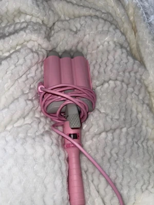 Rosa vågtång för hår - Säljer en rosa vågtång för hår med tre cylindrar och grå detaljer. Perfekt för att skapa snygga beach waves. Tången har ett greppvänligt handtag och en lång sladd. Enkel att använda för att fixa frisyren hemma. Använd endast 3 gånger!!