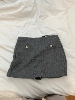 Svartvita skorts med fiskbensmönster - Snygga skorts i svartvitt fiskbensmönster med två dekorativa fickor bak och vita knappar. Klassisk och trendig look, perfekt för dig som gillar stilrena detaljer. Materialet känns mjukt och har en lätt struktur.