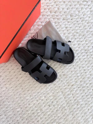 Svarta  sandaler  - Säljer ett par svarta sandaler som jag fått i present i stilren design med breda remmar i läder och ikoniskt H-mönster. Perfekta för en trendig och avslappnad look. Kommer med originalförpackning och dustbag. Jag är storlek 40 och dessa är för små tyvärr även om fet står att storleken är 40. De passar snarare 39-39,5