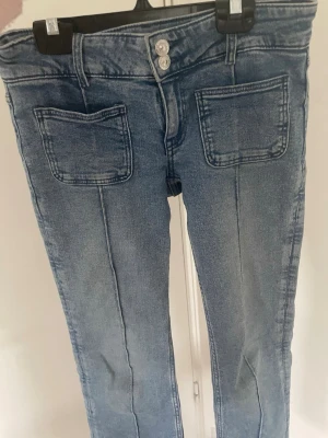 Ljusblå jeans med bootcut ben - Säljer ett par ljusblå jeans med bootcut ben och markerade sömmar framtill. Jeansen har två stora fickor fram och dubbla knappar i midjan. Perfekta för en avslappnad och trendig look.💕🌸💐