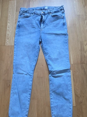Ljusblå skinny jeans med hög midja - Säljer ett par ljusblå skinny jeans med klassisk femficksdesign och hög midja. Jeansen har dragkedjegylf och knapp, samt guldfärgade nitar vid fickorna. Perfekta för en avslappnad och trendig look.