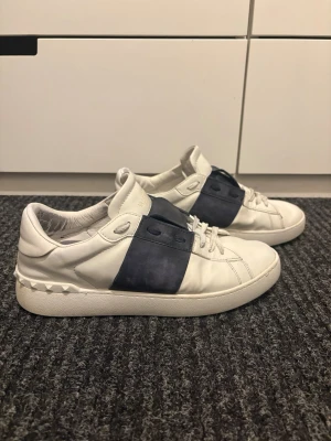 Valentino Garavani vita sneakers - Valentino sneakers - strl 43 Vita Valentino-sneakers i skinn med marinblå detalj i mocka. Använda men i bra skick, se bilder för vanligt slitage. Säljer dem eftersom de inte passar mig längre. 📏Storlek 43 💶Pris kan diskuteras 📦Skickas snabbt