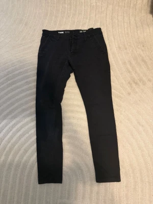 Svarta chinos från G-Star RAW - Snygga svarta chinos från G-Star RAW i klassisk rak modell. Byxorna har diskreta fickor fram och bak samt bälteshällor. Tillverkade i mjukt bomullsmaterial med en stilren look som passar perfekt till många olika outfits.