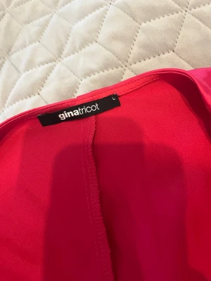 Röd satinblus från Gina Tricot - Snygg röd blus från Gina Tricot i glansigt satinmaterial. Modellen har långa ärmar och smockad midja som ger en trendig och bekväm passform. Perfekt för dig som vill sticka ut med en färgstark topp.