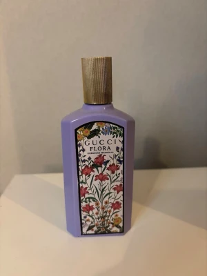 Gucci Flora Gorgeous Magnolia parfym - Gucci Flora Gorgeous Magnolia är en parfym i en lila, rektangulär flaska med guldfärgad kork. Framsidan har en färgglad blommig etikett med märkets logga. Den är helt full, endast testad