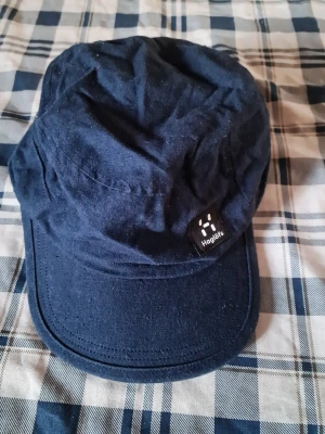 Mörkblå keps från Haglöfs - Snygg mörkblå keps från Haglöfs i mjukt tygmaterial. Klassisk form med böjd skärm och diskret logotyp framtill. Perfekt accessoar för en avslappnad och sportig stil.