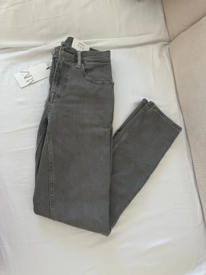 Grå slim fit jeans från Zara - Snygga grå slim fit jeans från Zara med klassisk femficksdesign och dragkedjegylf. Jeansen har en modern passform och är tillverkade i mjuk denim med lite stretch för extra komfort. Perfekta för en trendig och avslappnad look.