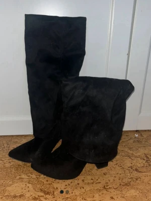 Svarta höga mockastövlar - Snygga svarta stövlar i mocka imitation med låg klack. Stövlarna har en klassisk, stilren design med spetsig tå och passar perfekt till jeans eller kjol. Materialet är mjukt och ger en lyxig känsla. Perfekta för dig som vill ha en trendig look.