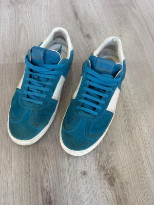Valentina Flycrew - Snygga sneakers från Valentino flycrew i blå mocka och vitt läder. Skorna har blå skosnören, vit sula och klassisk låg siluett. Perfekta för dig som gillar en sportig och stilren look med premiumkänsla. Det fattas en nit som har lossnat av sig själv. 