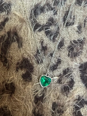 Halsband med grönt hjärthänge spjut silver - Snyggt halsband i silverfärgad metall med ett hjärtformat grönt hänge. Hänget har en pil genom sig och kedjan är tunn och stilren. Perfekt för dig som gillar unika smycken med färg och cool design. Rostfri 