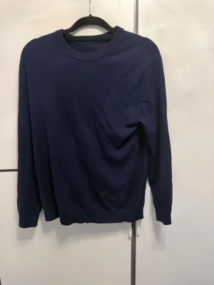 Mörkblå John Henric Kashmir tröja  - En enkel och stilren mörkblå john Henric tröja med rund halsringning och långa ärmar. Perfekt att matcha med jeans  för en clean look. Tröjan har ribbade muddar vid ärmslut och nederkant. Materialet ser ut att vara mjukt och bekvämt.