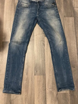 Blå raka jeans med slitningar - Snygga blå jeans med raka ben och slitna detaljer framtill och baktill. Klassisk femficksmodell med ljusa partier på låren och knäna. Jeansen har en normalhög midja och är tillverkade i denim. Perfekta för en avslappnad och trendig look.