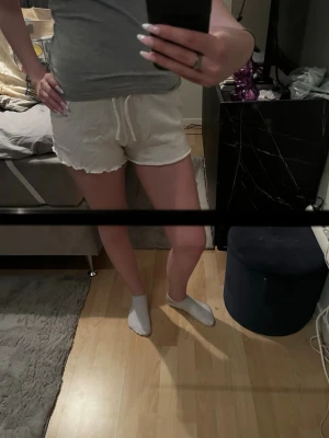Vita shorts med snörning - Säljer ett par vita shorts med snörning i midjan och vågig kant nertill. De är lätta och perfekta för varma dagar, med en avslappnad passform och mjukt material. Passar perfekt till sommarens alla outfits.
