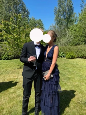 Marinblå långklänning med volanger - Snygg marinblå långklänning med djup v-ringning och volangdetaljer i flera lager. Klänningen är öppen i ryggen och perfekt att ha till bröllop eller balen. Använd en gång och jag är 173 cm lång