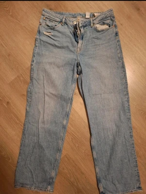 Ljusblå raka jeans med coola hål - Säljer ett par ljusblå jeans med raka ben och små slitningar vid fickorna. Klassisk femficksmodell med dragkedja och knapp. Jeansen har en avslappnad passform och är tillverkade i denim. Perfekta för en casual look.