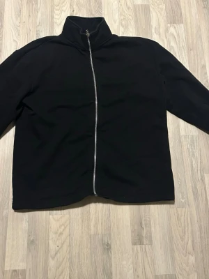 Svart jacka med hög krage och dragkedja - Stilren svart jacka med hög krage och hel dragkedja framtill. Jackan har en minimalistisk design och är perfekt för dig som gillar en clean look. Långärmad och passar bra till lager-på-lager-stil.