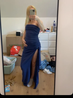 Marinblå långklänning med slits - Säljer en marinblå axelbandslös långklänning med hög slits på ena sidan. Klänningen har en figurnära passform och är perfekt för dig som vill ha en elegant och stilren look. Materialet känns mjukt och följsamt mot kroppen.