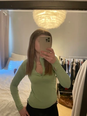 Ljusgrön långärmad polotopp - Snygg ljusgrön långärmad polotopp med half zip framtill. Toppen har en slim passform och är perfekt för dig som gillar en enkel och stilren look. Materialet känns mjukt och stretchigt, vilket gör den bekväm att bära hela dagen.