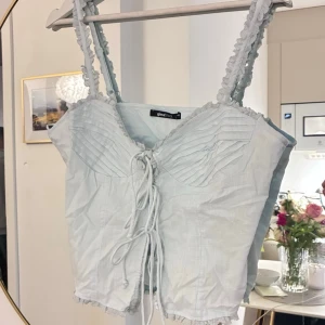Ljusblå linnetopp med snörning - Supersöt ljusblå linnetopp från Gina Tricot med dekorativa axelband och snörning framtill. Toppen har en lätt rynkad byst och fina detaljer längs kanterna. Perfekt att styla med jeans eller kjol för en trendig look. Med prislapp! Ord pris 259kr