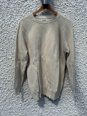 Beige stickad tröja från SAMS - Snygg beige stickad tröja från SAMS i storlek L. Tröjan har rund halsringning, långa ärmar och ribbade muddar vid ärmslut och nederkant. Perfekt för lager-på-lager och enkel att matcha med andra plagg.
