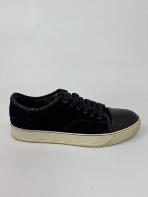 Svarta Lanvin sneakers med mockadetaljer - Snygga svarta sneakers med ovandel i mocka och tåparti i slätt läder. Skorna har svarta skosnören och en vit, klassisk gummisula. Perfekta för dig som gillar stilrena och tidlösa sneakers med en twist.