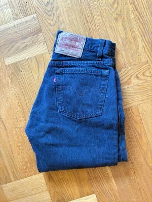 Levi's 501 grå/svarta raka jeans - Klassiska Levi's 501 jeans denim med raka ben och hög midja. Jeansen har fem fickor, knappgylf och den ikoniska läderpatchen bak i midjan. Perfekta för en tidlös och avslappnad stil.