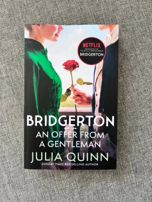 Bridgerton: An Offer From a Gentleman - En romantisk roman på engelska av Julia Quinn, tredje delen i Bridgerton-serien. Omslaget är färgstarkt med motiv av två personer och en röd ros. Boken är i pocketformat och har en koppling till Netflix-serien Bridgerton.