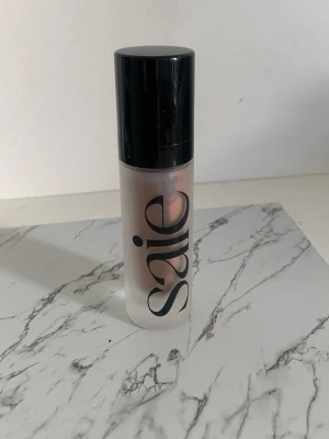 Saie flytande bronzer i pumpflaska - Flytande bronzer från Saie i en stilren, frostad pumpflaska med svart lock. Produkten har en naturlig, varm ton och är enkel att applicera tack vare pumpen. Perfekt för att ge huden en solkysst look och glow.
