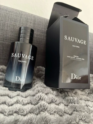 Dior Sauvage Eau Forte Parfym - Dior Sauvage Eau Forte är en elegant parfym i en stilren svart glasflaska med vit logotyp. Flaskan har en rund form och ett svart lock med Dior-loggan på toppen. Kommer i originalkartong. Perfekt för dig som gillar exklusiva dofter.