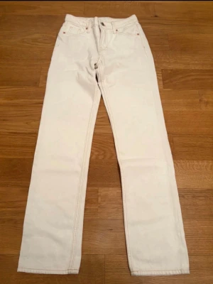 Vita raka jeans från Levi's - Säljer ett par vita jeans från Levi's med rak passform och klassisk femficksdesign. Jeansen har hög midja och är tillverkade i ett kraftigt bomullstyg. Perfekta för dig som vill ha en clean och stilren look.