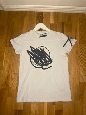 Vit t-shirt med tryck - Vit t-shirt med rund hals och korta ärmar. Framsidan har ett tryck i mitten. Enkel och klassisk modell som passar till det mesta. Tillverkad i mjukt bomullsmaterial.