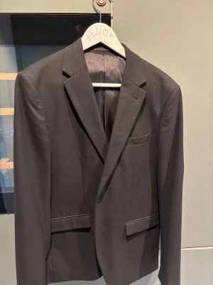 Klassisk svart kavaj och kostymbyxor! Strl 44! - En stilren svart kavaj med två framfickor och bröstficka. Kavajen har smal passform, enkelknäppt design och klassiska slag. Perfekt för en dressad look och funkar till skjorta eller t-shirt. Materialet känns slätt och lätt, vilket ger en snygg siluett. Kostymbyxor i samma storlek (44) ingår i priset. Om du vill köpa endast kavajen eller byxorna så hör av dig! Perfekta valet inför skolavslutning och annat, så man slipper köpa nytt som helt enkelt bara tar plats i garderoben :) Anvönd 1 gång.