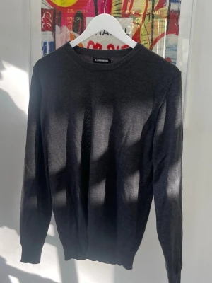 Mörkgrå stickad tröja J.Lindeberg - Snygg mörkgrå stickad tröja från J.Lindeberg med rund halsringning och långa ärmar. Tröjan är tunnstickad och har en stilren, minimalistisk design som passar perfekt till lager-på-lager. Materialet känns mjukt och följsamt.