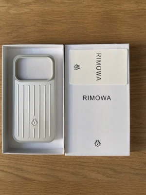 Rimowa silverfärgat mobilskal iphone 17 pro max - Stilrent mobilskal från Rimowa i silverfärgad aluminium med ikoniska räfflade linjer. Skalets design är inspirerad av Rimowas klassiska resväskor och har en robust känsla. Passar perfekt för dig som vill ha ett exklusivt och modernt skydd till din mobil.