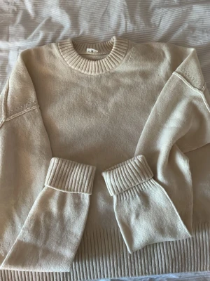 Beige stickad tröja med breda muddar - Snygg beige stickad tröja med rund hals och breda ribbade muddar vid ärmslut och nederkant. Tröjan har en avslappnad passform och är perfekt för lager-på-lager. Materialet känns mjukt och bekvämt mot huden.