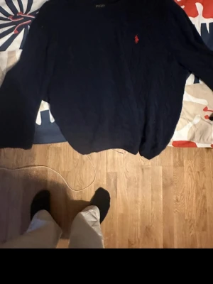  Tröja Polo Ralph Lauren  - Knappt använd, Mörkblå tröja från Polo Ralph Lauren med rund hals och röd broderad logga på bröstet. Tröjan är stickad och har långa ärmar, perfekt för en klassisk och stilren look.