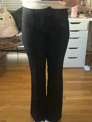 Svarta utsvängda kostymbyxor - Snygga svarta kostymbyxor med utsvängda ben och pressveck framtill. Byxorna har hög midja och fickor bak med lock. Perfekta för en stilren och trendig look.