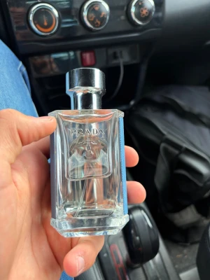 Prada L'Homme Eau de Toilette - Snygg parfymflaska från Prada med silvrigt lock och ljusblått läderomslag. Flaskan är genomskinlig med Pradas logga ingraverad på framsidan. Perfekt för dig som gillar exklusiva och stilrena dofter. OBS: Fick en ny parfym av päronen så säljer den halvfull. :)