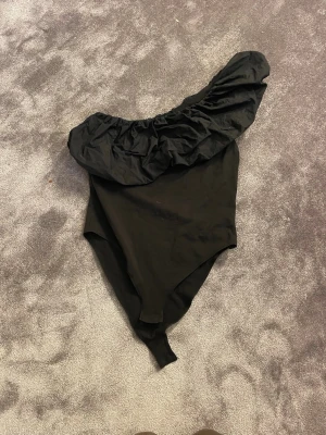 Svart body med volang - Supersnygg svart body med en axel och stor volangdetalj. Väldigt fin fest body men även till vardags. Från Anna Feild