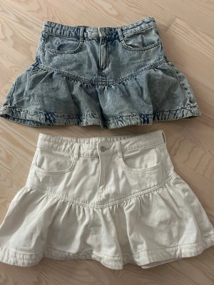 Två volangkjolar i denim och vitt - Två korta kjolar med volang, en i ljusblå denim och en i vit bomull. Båda har fickor fram och markerad söm vid volangen. Perfekta för en trendig och avslappnad stil.