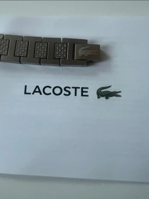 Lacoste armband - Stilrent armband i silverfärgat stål med rektangulära länkar. Varje länk har en unik design med både blanka och mönstrade ytor. Perfekt accessoar för dig som gillar minimalistisk och modern stil.