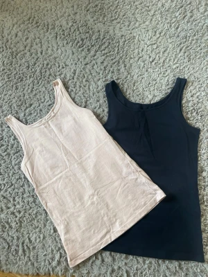 2-pack baslinnen i svart och beige - Två stilrena baslinnen i mörkblått och ljusrosa, perfekta att matcha till olika outfits. Båda är ärmlösa med klassisk rund halsringning och har en slim passform. Materialet känns mjukt och stretchigt, vilket gör dem bekväma att bära hela dagen. Storlek 158/164 men skulle säga att de passar xs/s💕 pris kan diskuteras vid snabb affär