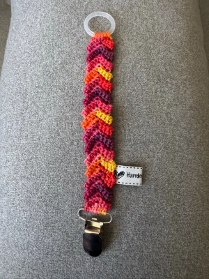 Virkad napphållare  - Virkad, flerfärgad napphållare i rött/gult/lila. Virkad av mig i 100% bomullsgarn med metallclip och silikonring.  Mönsterskapare: animo.design