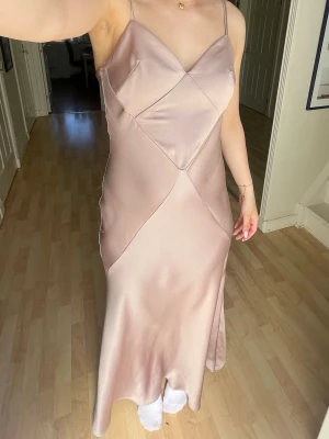 Champagnefärgad långklänning i satin - Elegant långklänning i champagnefärgad satin med smala axelband och figurnära passform. Perfekt balklänning💗Klänningen har en v-ringad urringning och dekorativa sömmar framtill som ger en modern look! Min Chiquelle balklänning från 9an som bara kommit till användning den gången, därav säljer jag!💞Nypris 1 300kr💗