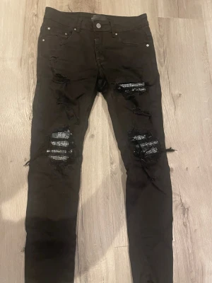 Amiri  - Svarta skinny jeans med coola slitningar och trasiga detaljer över knäna. Jeansen har klassisk femficksdesign och silverfärgade nitar. Perfekt för en edgy streetstil.