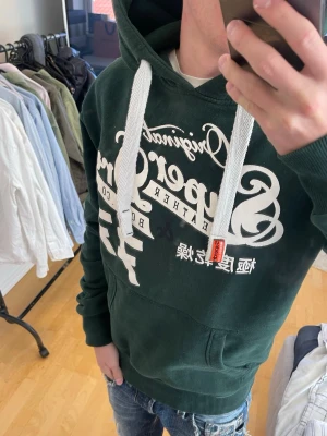 Grön Superdry hoodie med tryck - Säljer nu denna sjukt snygga Vintage 2000s SuperDry hoodie! Passar till allt och har en perfekt passform. Säljs ej längre i butik och är därav mycket eftertraktad😊 Skriv vid funderingar 🤝