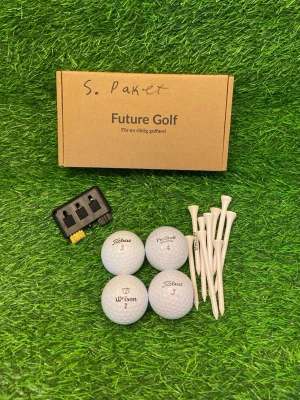Golfkit med bollar, peggar och borste, startpaket för nybörjare - Golfkit från Future Golf med fyra vita golfbollar från Titleist, Wilson och ProStaff, vita peggar samt en svart borste för rengöring av klubbor. Allt levereras i en brun kartong med text. Perfekt för golfentusiasten som vill ha allt samlat.