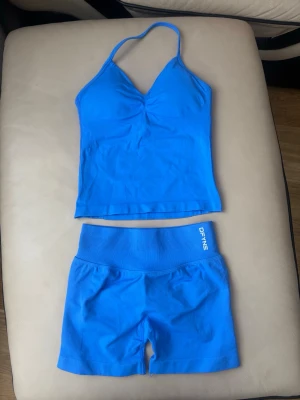 Blått set från Dfyne med topp och shorts - Säljer ett blått set från Define med en tight halterneck-topp och matchande shorts. Setet är sömlöst och gjort i stretchigt material som sitter skönt mot kroppen. Perfekt för dig som gillar sportig och stilren look.