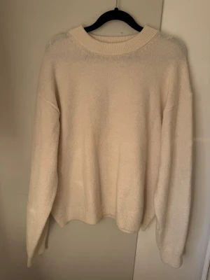 Beige stickad tröja från H&M - Mysig beige stickad tröja från H&M med rund halsringning och avslappnad passform. Tröjan har långa ärmar och ribbade muddar vid hals, ärmslut och nederkant. Perfekt för lager på lager och enkel att matcha med olika outfits.