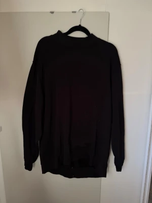 Svart oversized hoodie - En enkel svart oversized hoodie med långa ärmar och ribbade muddar vid ärmslut och nederkant. Hoodien har en klassisk passform utan synliga loggor eller tryck och är tillverkad i ett mjukt bomullsliknande material. Perfekt för en chill och avslappnad stil.
